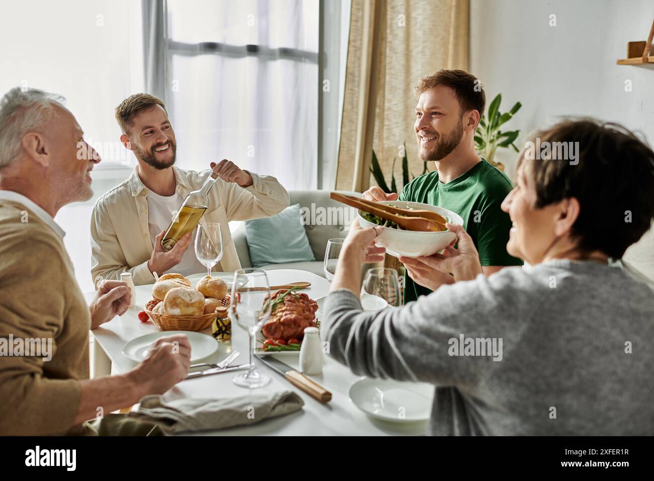 Una coppia gay gode di un pasto con i genitori a casa. Foto Stock