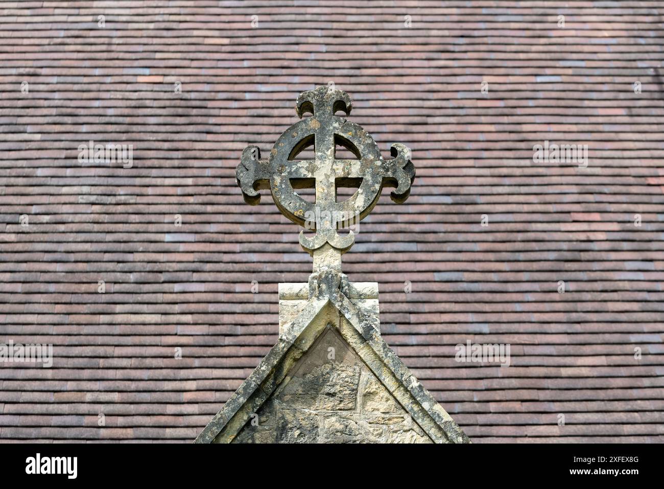 Croce di pietra sopra l'ingresso di una chiesa con piastrelle del tetto fuori fuoco dietro. Questa è la chiesa della Santa Croce vicino a Ryde. Luglio 2024 Foto Stock