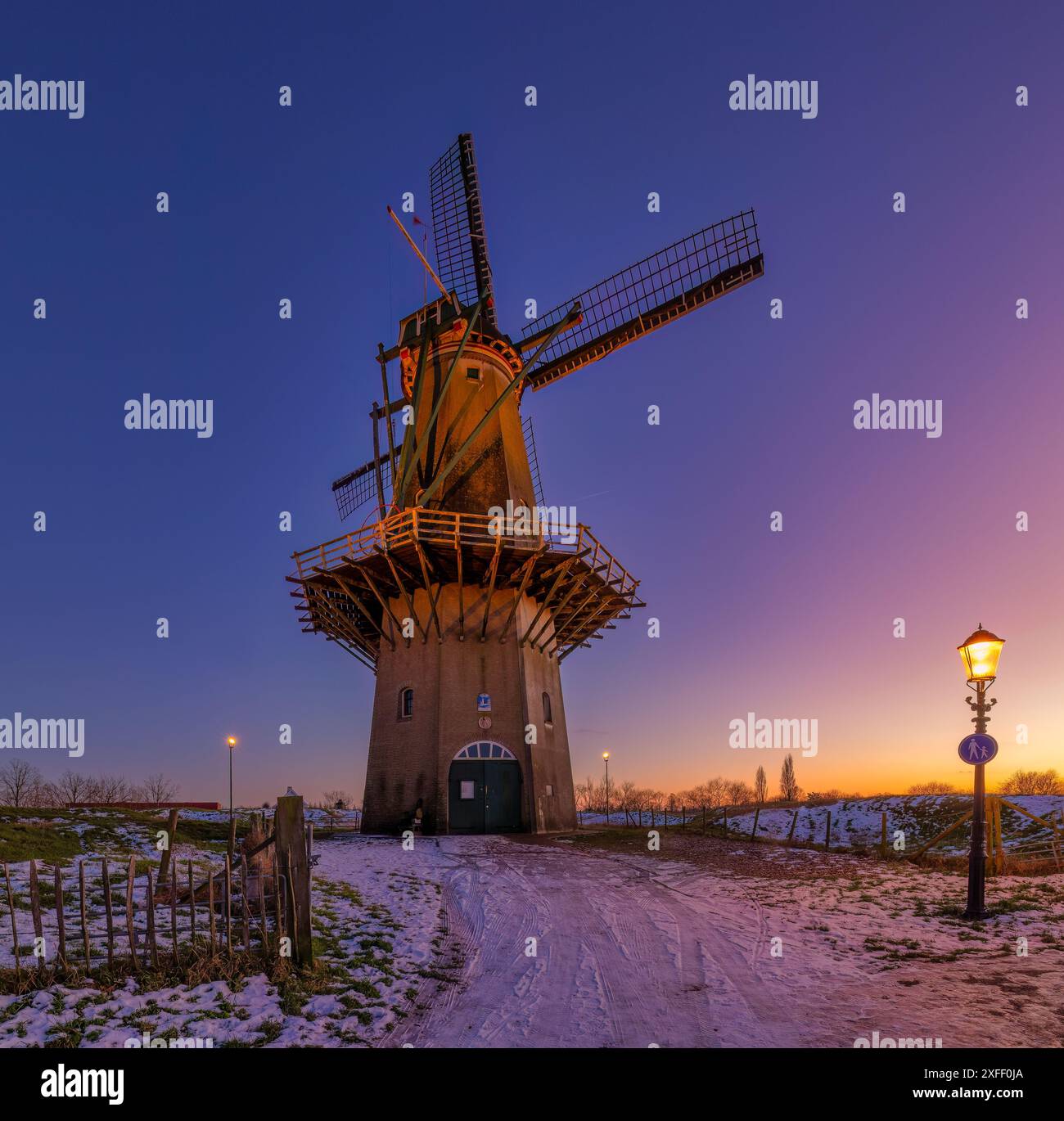 Un tradizionale mulino a vento olandese nei Paesi Bassi in inverno con neve e un vibrante tramonto con splendidi colori - una splendida immagine di viaggio Foto Stock