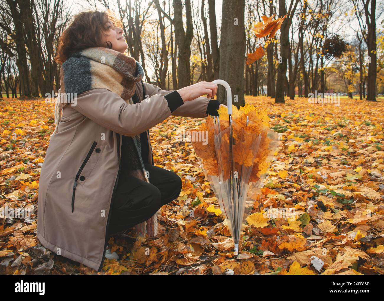 una donna di 50 anni cammina nel parco in autunno in una calda giornata di sole, guarda le foglie che cadono e ride Foto Stock