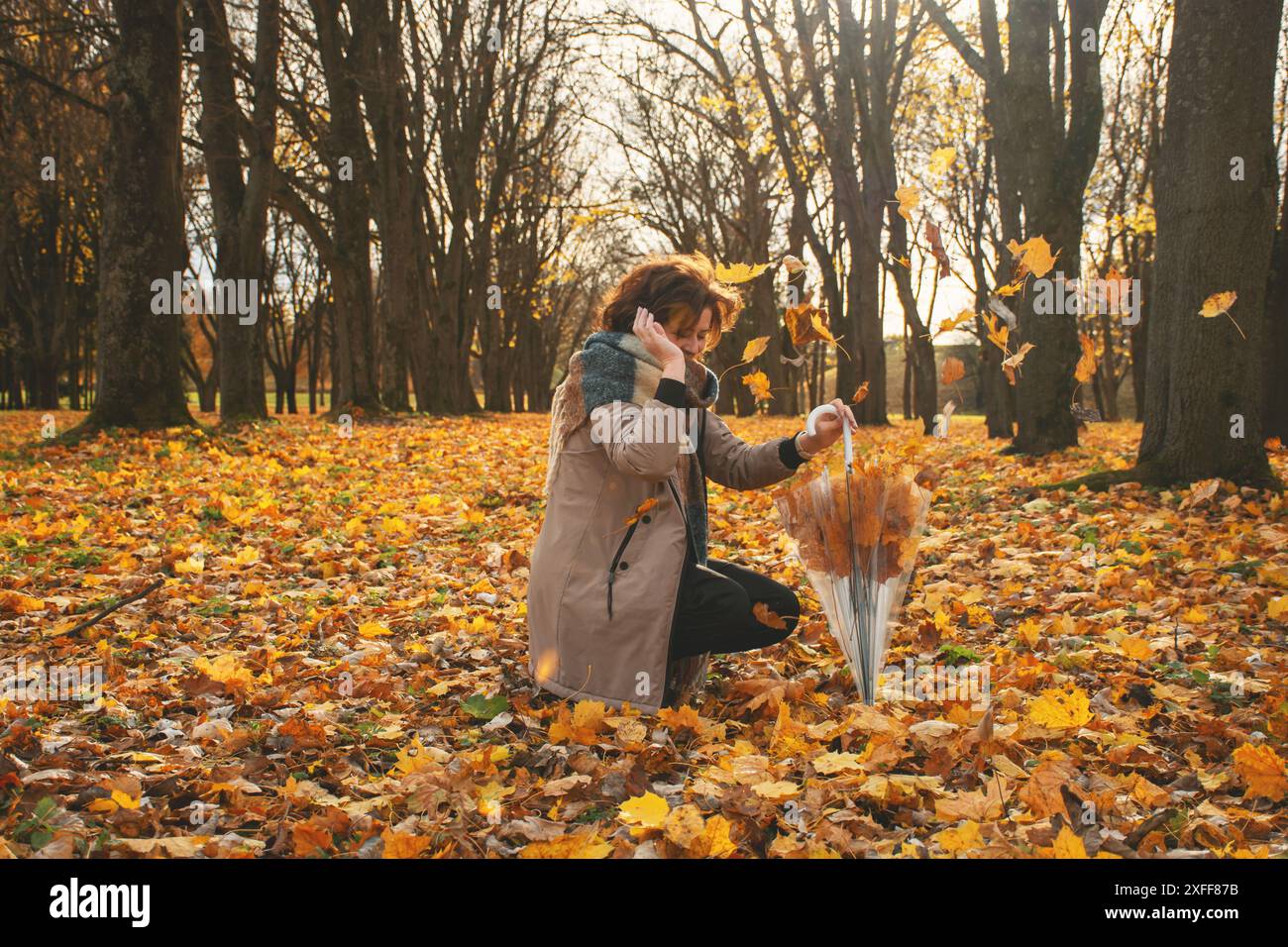 una donna di 50 anni cammina nel parco in autunno in una calda giornata di sole, si toglie le foglie cadenti e ride Foto Stock