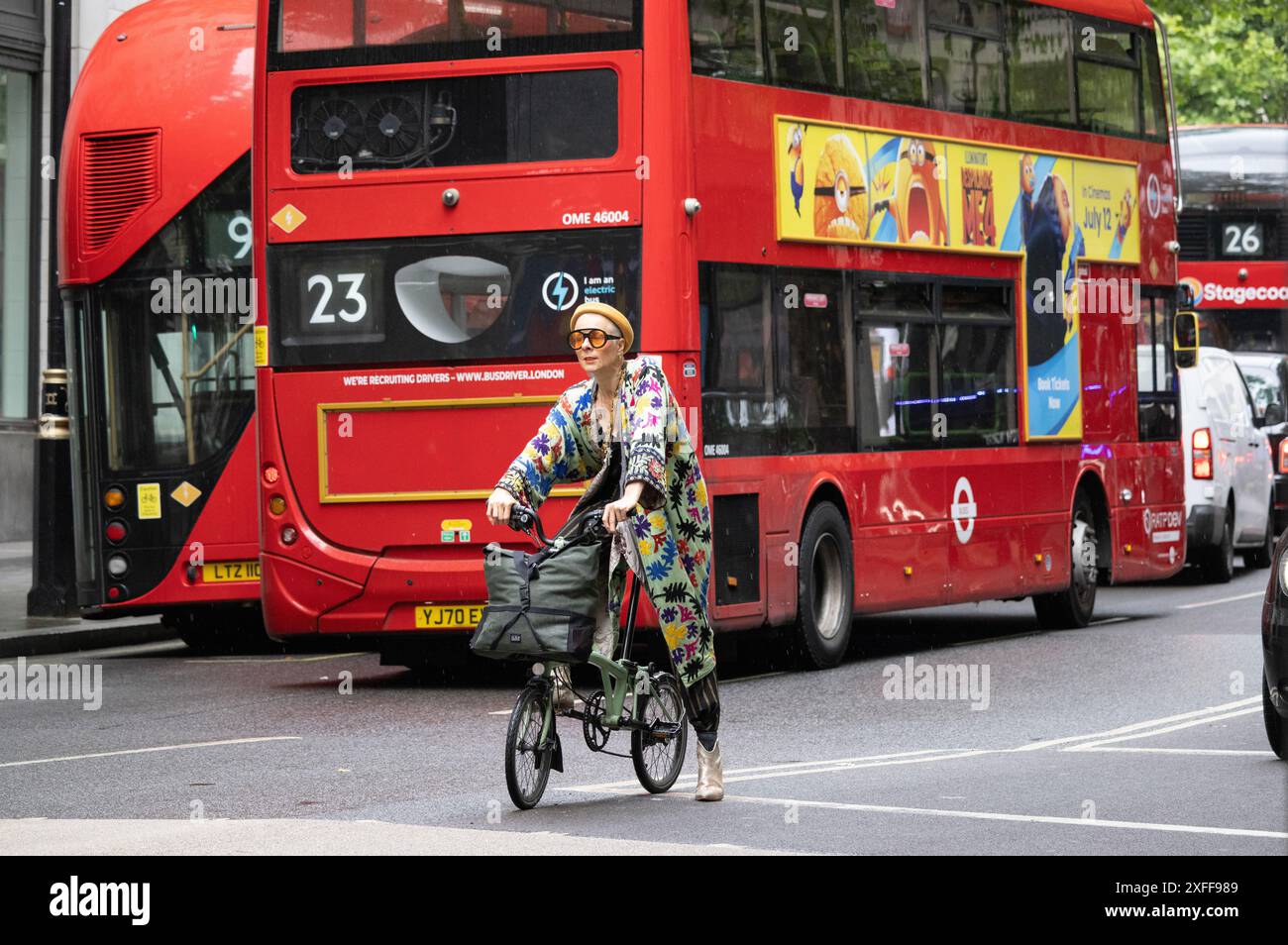 Un pendolare colorato che indossa abiti alla moda siede sulla sua bici da città di Brompton tra il traffico di Aldwych, nel centro di Londra, Inghilterra, Regno Unito Foto Stock