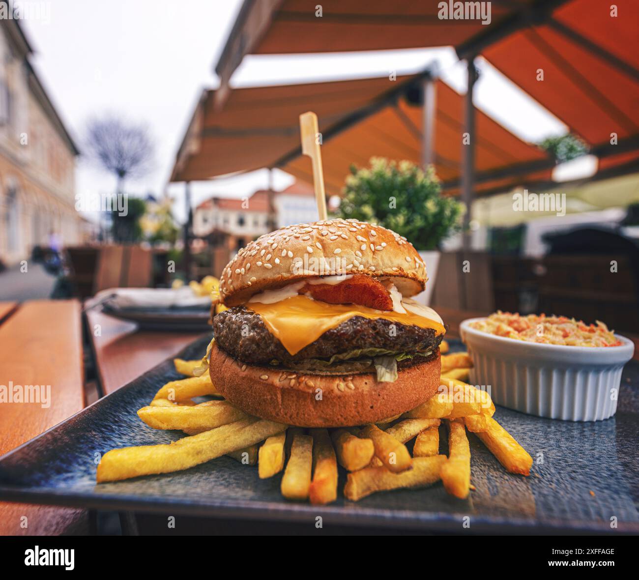 Cheeseburger fresco con polpette di carne, formaggio, salsa e insalata servito su panino con patatine fritte sul piatto Foto Stock