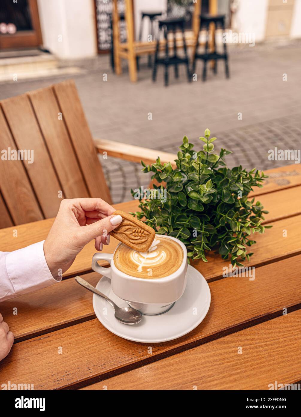 Donna che immerge un biscotto nel suo cappuccino mentre siede in un bar all'aperto Foto Stock Donna che immerge un biscotto nel suo cappuccino mentre siede in un bar all'aperto Foto Stock