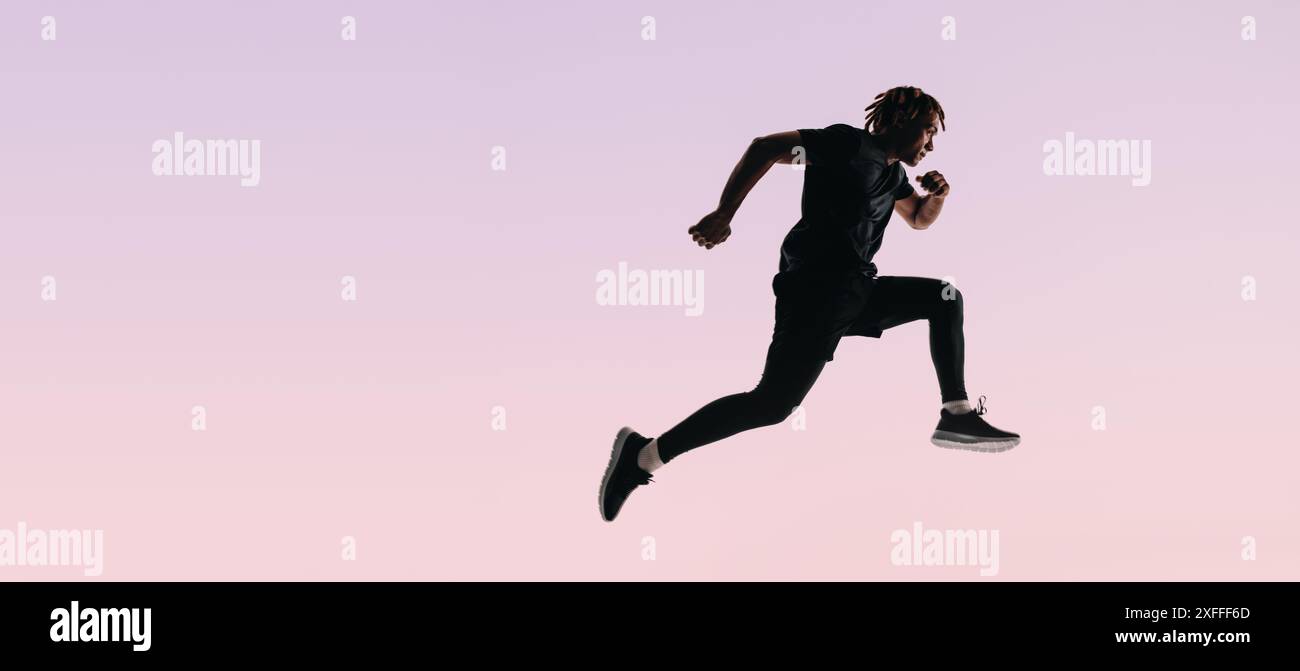 Giovane atleta con dreadlock salta su uno sfondo rosa. La sua silhouette a tutta lunghezza cattura la sua forma fisica e il suo stile di vita sano. Foto Stock