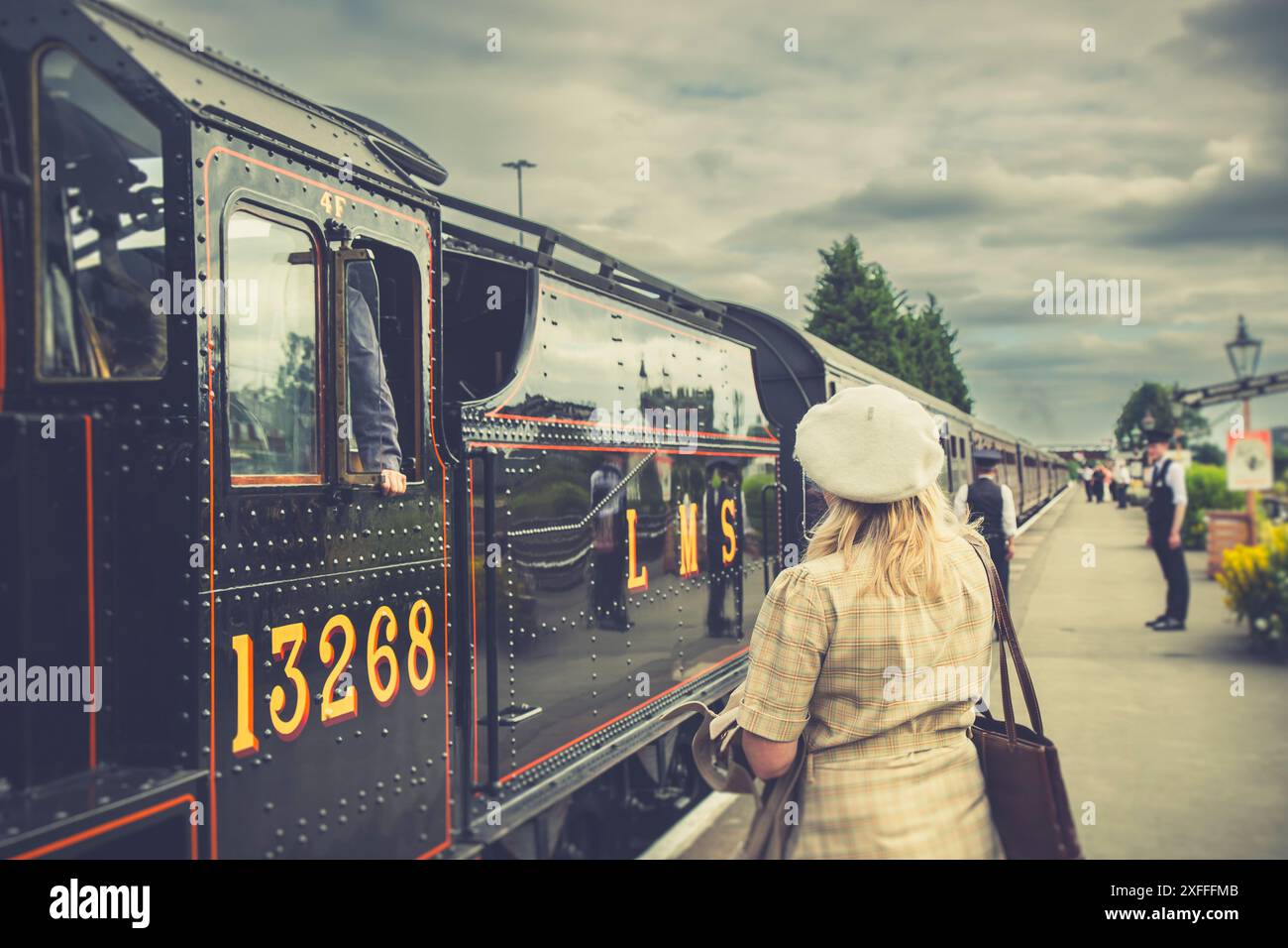 Vista posteriore di una donna che indossa un cappello su una piattaforma ferroviaria con una locomotiva a vapore in stazione durante il fine settimana degli anni '1940 presso la stazione ferroviaria della Severn Valley Railway di K. Foto Stock