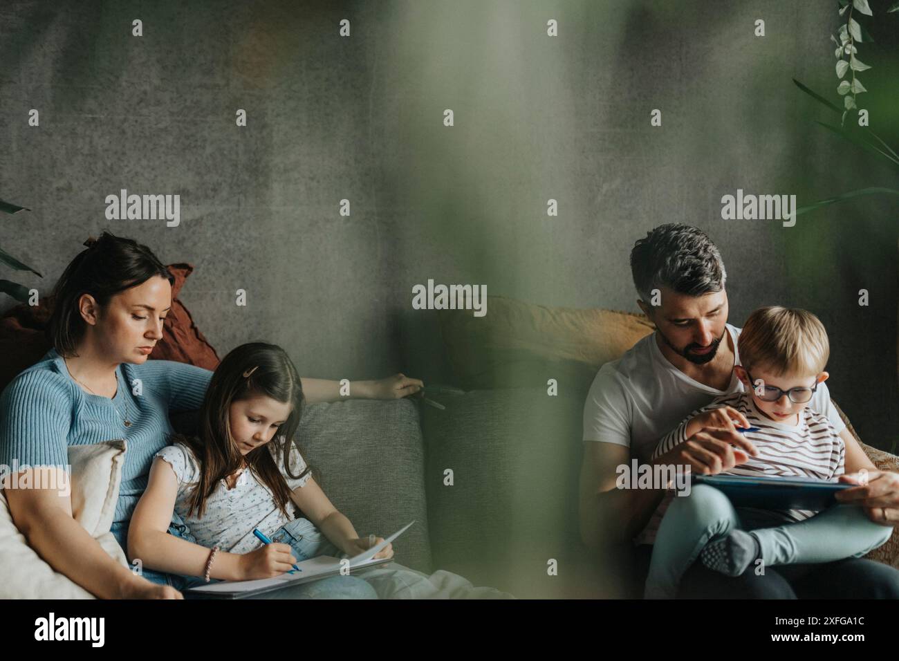I genitori che studiano a casa, figlio e figlia seduti sul divano a casa Foto Stock
