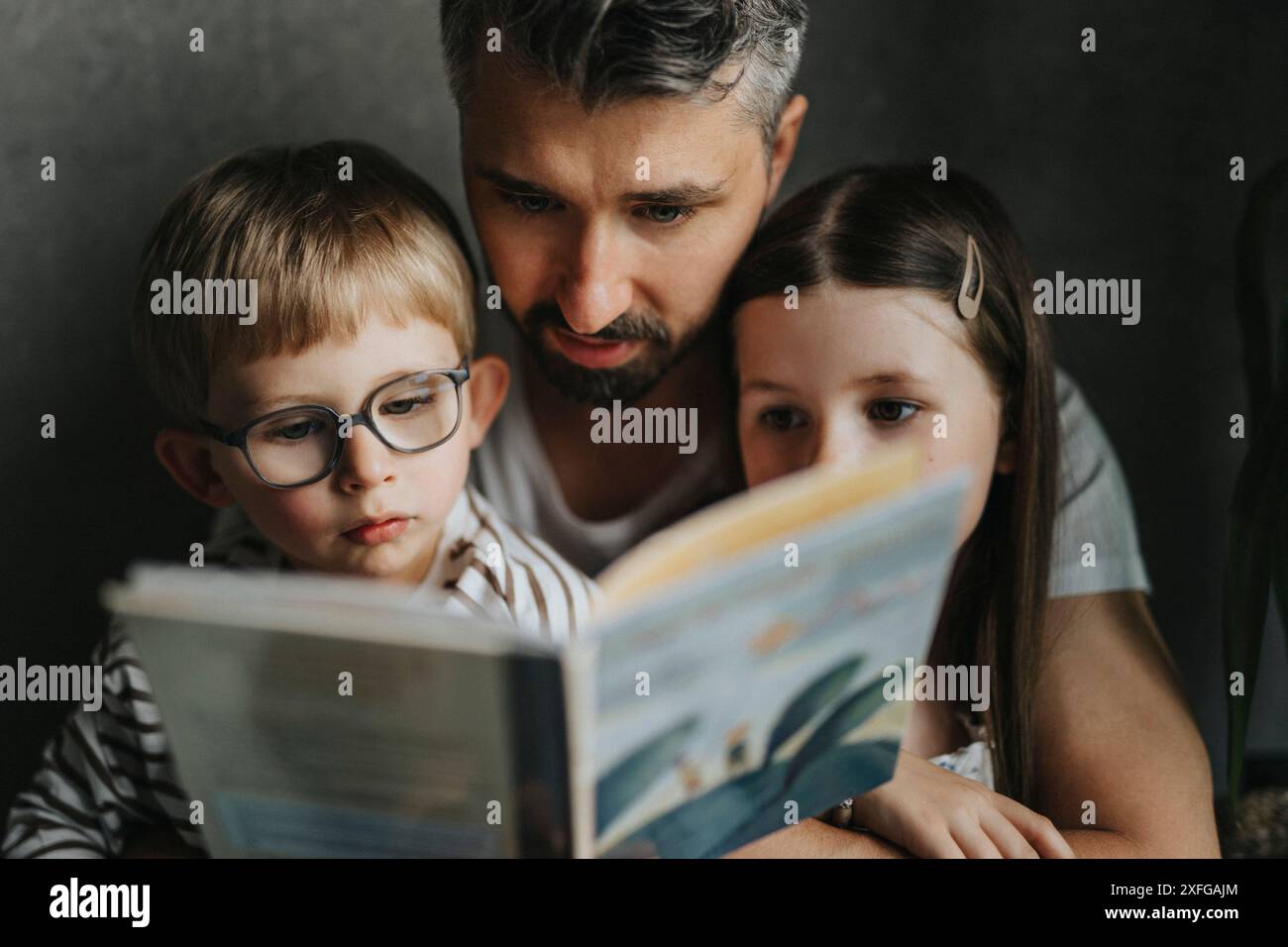 Padre che legge un libro con figlio e figlia a casa Foto Stock