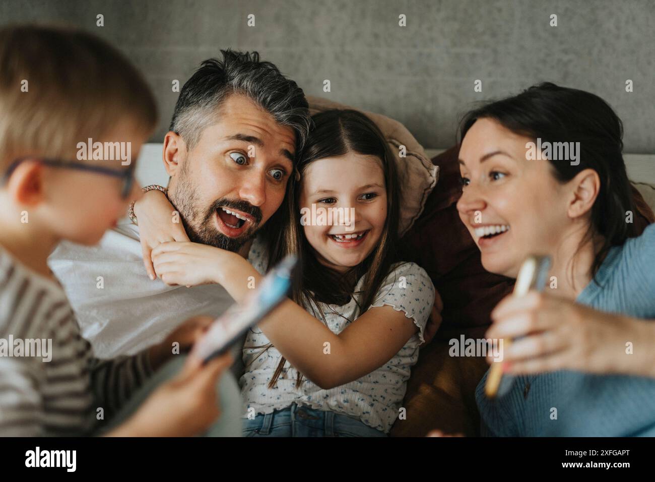 Una famiglia allegra che trascorre il tempo libero con gli smartphone a casa Foto Stock