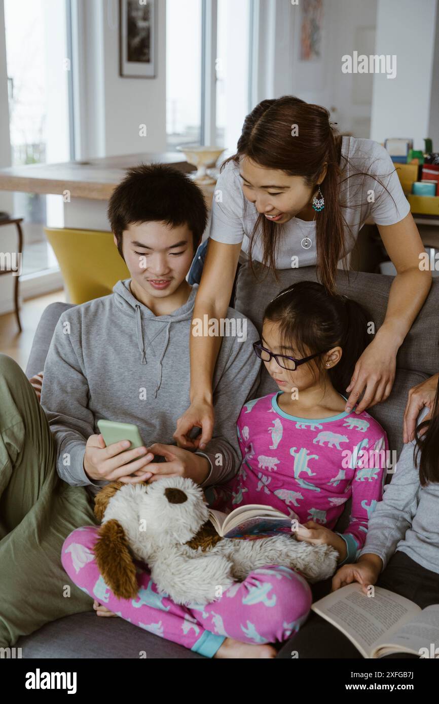 Donna seduta con figlio e figlia che usa lo smartphone a casa Foto Stock