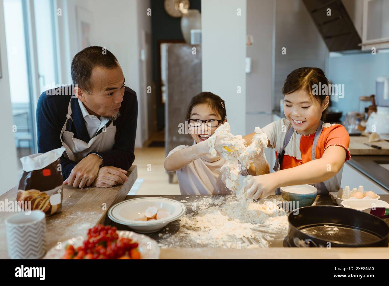 Padre che guarda le figlie che si divertono mentre cuoci in cucina a casa Foto Stock