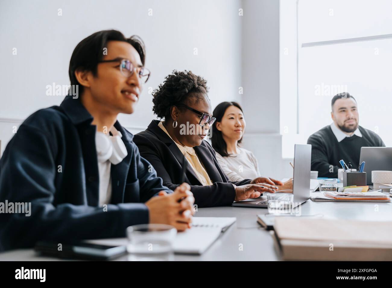 Donna d'affari matura che lavora con un notebook mentre è seduta con i colleghi in ufficio Foto Stock