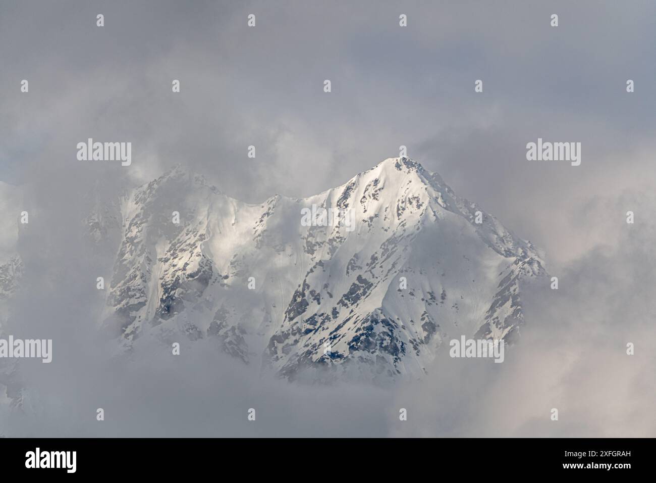 Nebbioso, cima di montagna ricoperta di neve nel nord del Canada, territorio dello Yukon con sfondo blu. Ideale per sfondi e visualizzazione desktop. Foto Stock