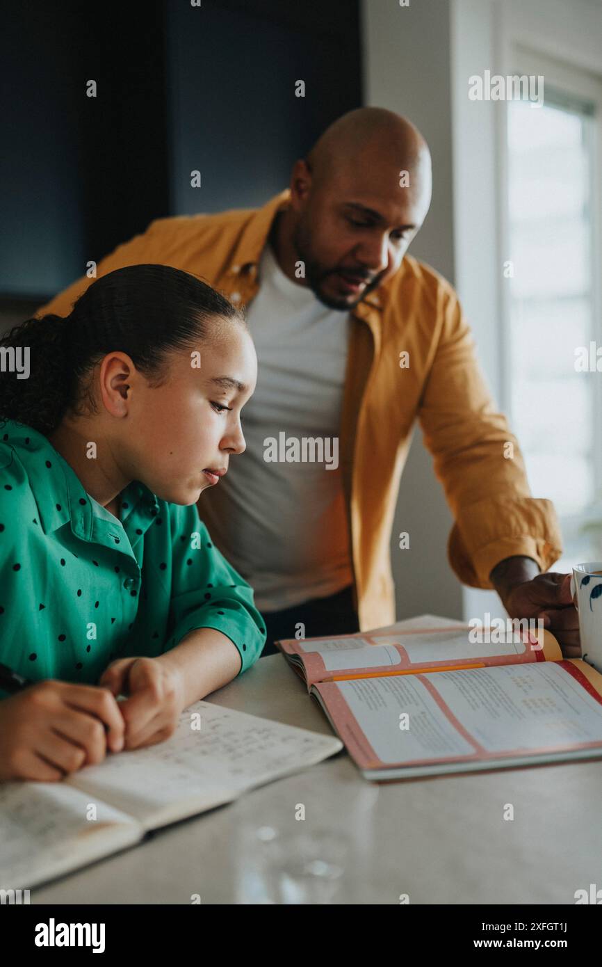 Padre che aiuta la figlia a leggere dal libro di testo a casa Foto Stock