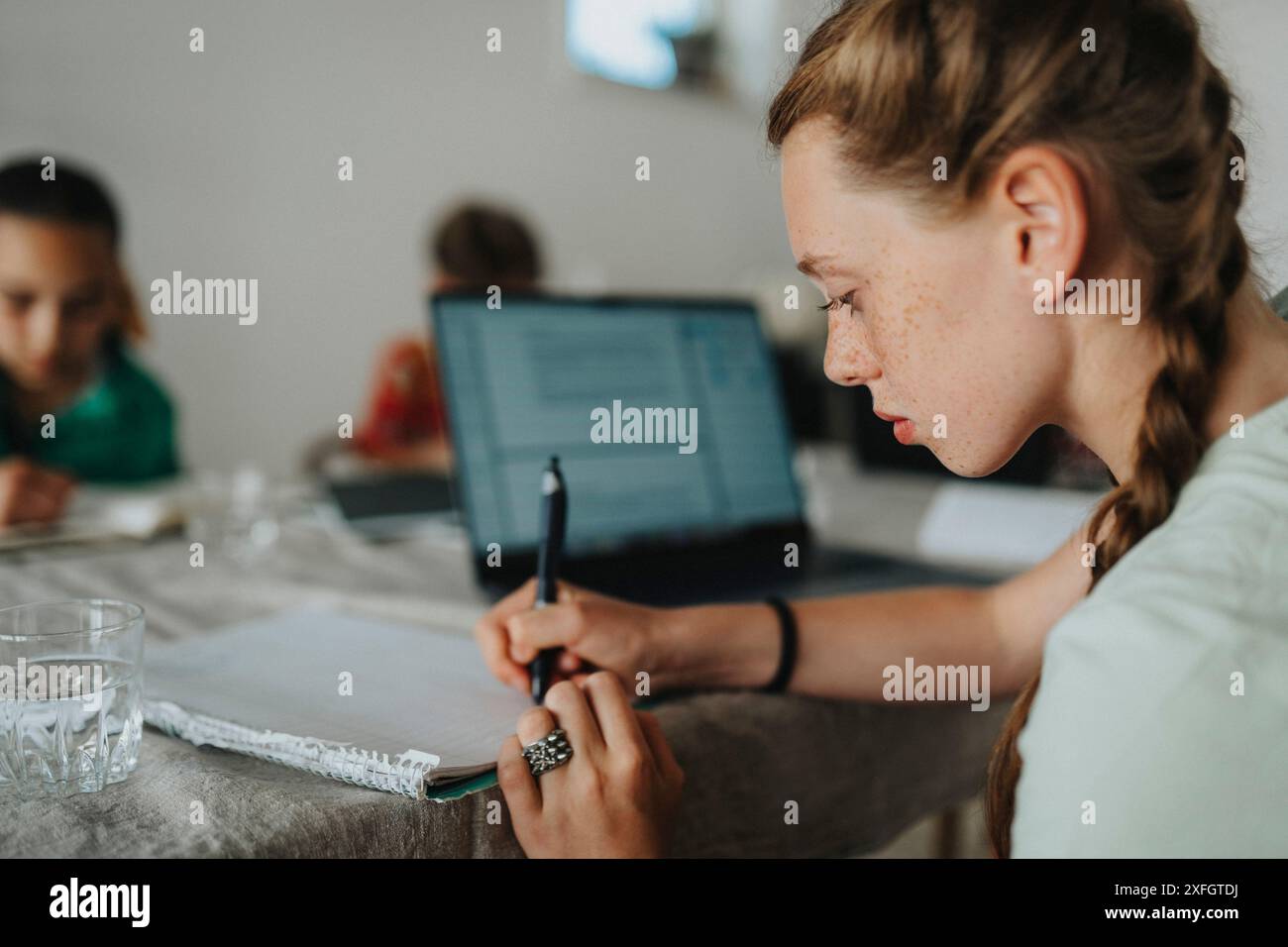 Ragazza con capelli intrecciati che scrive in diario mentre studia a casa Foto Stock