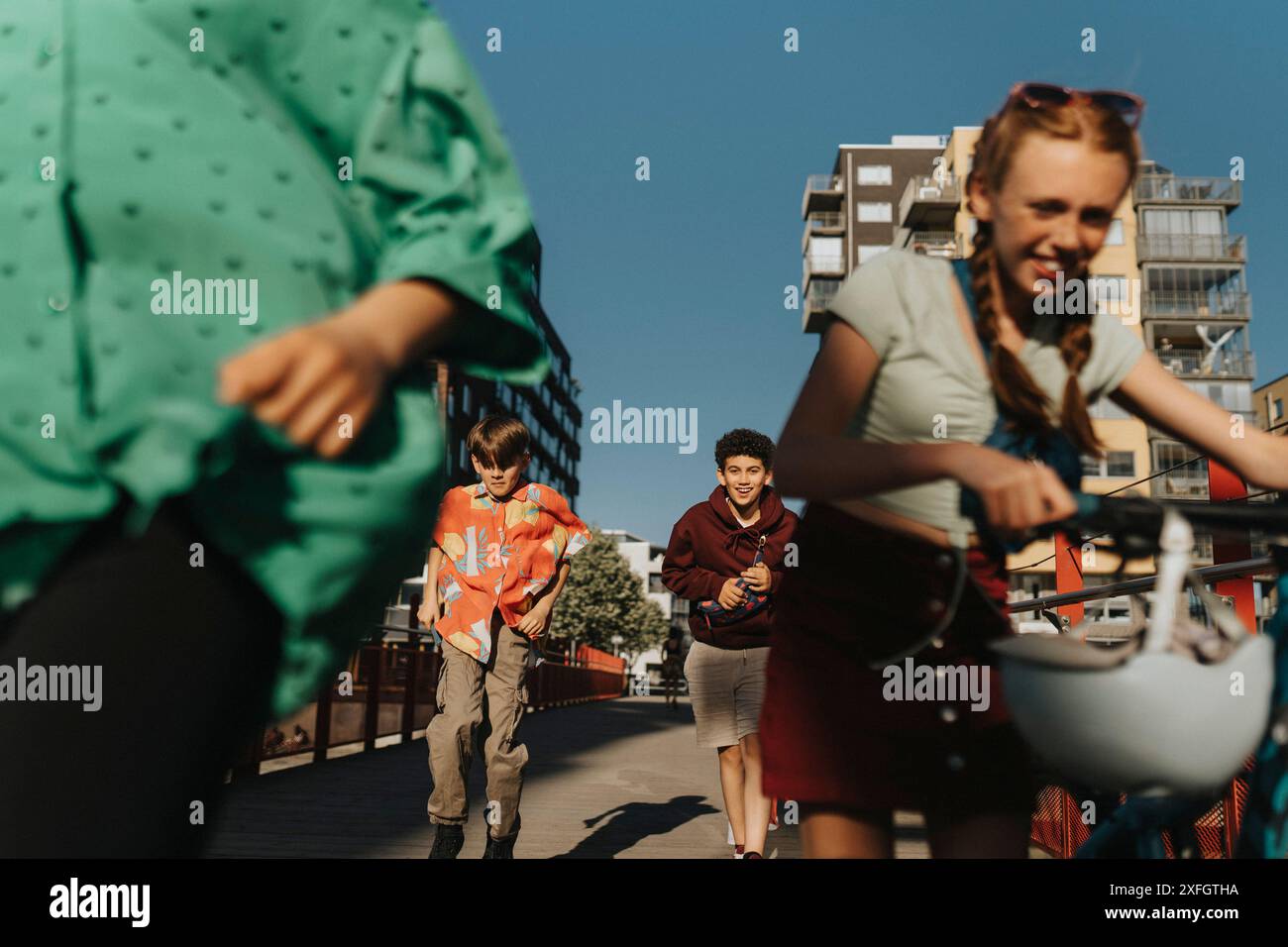 Amici maschi che corrono per strada mentre un'amica che cammina in bicicletta per strada Foto Stock