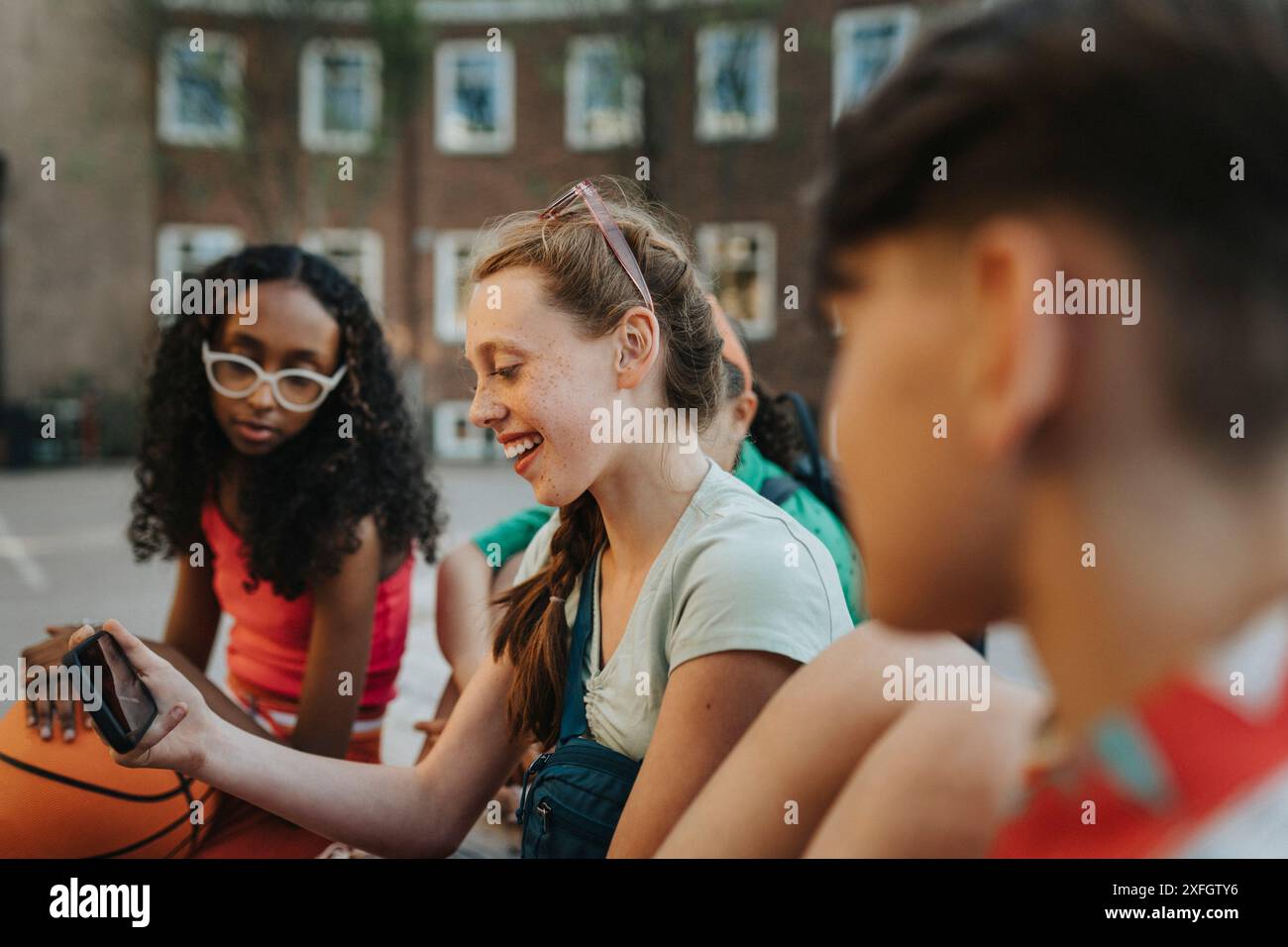 Ragazza felice che usa lo smartphone con gli amici al campus scolastico Foto Stock