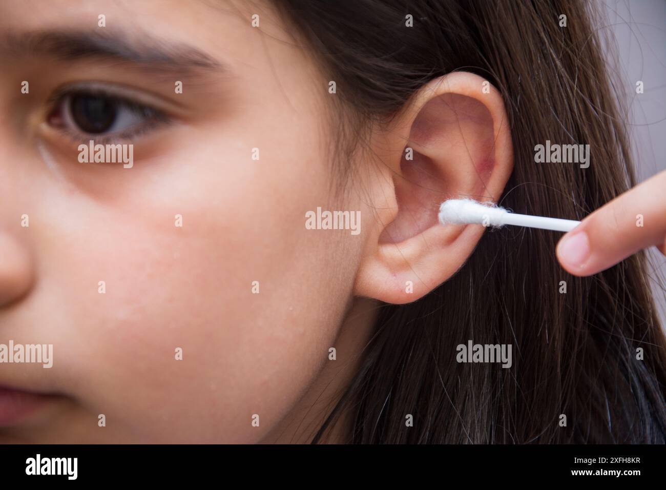 Bambina che pulisce l'orecchio con un bastoncino di cotone in primo piano Foto Stock