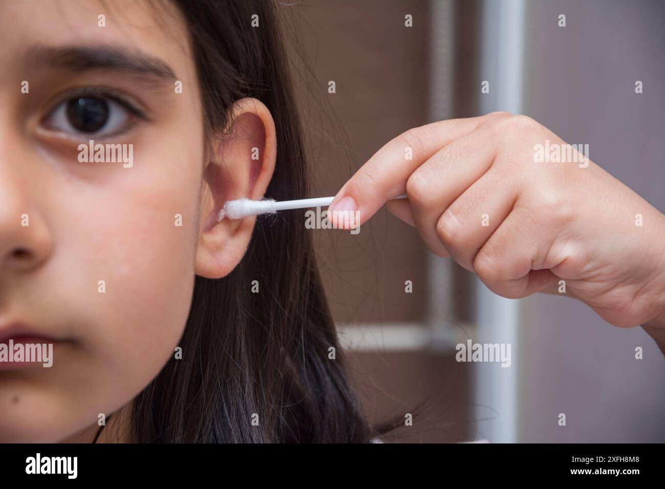 La bambina con metà del viso visibile pulisce l'orecchio con un bastoncino di cotone Foto Stock