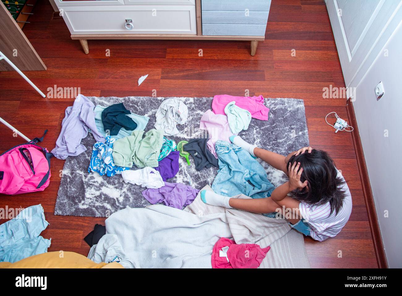 Vista dall'alto della bambina triste seduta sul pavimento nella sua stanza disordinata Foto Stock