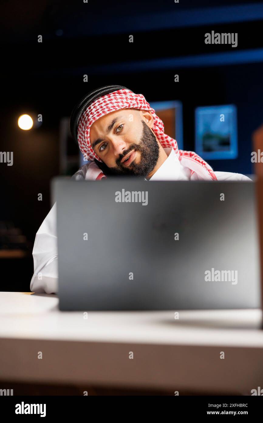 Una visione dettagliata di Muslim Guy si è concentrata sulla telefonata mentre esaminava il suo portatile. Professionalità e comunicazione eccellente sono esemplificate dalla persona araba che abbraccia la tecnologia. Primo piano. Foto Stock