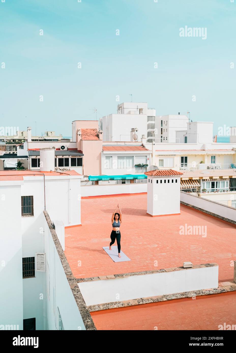 Vista distante della donna che fa yoga sulla terrazza dell'edificio Foto Stock