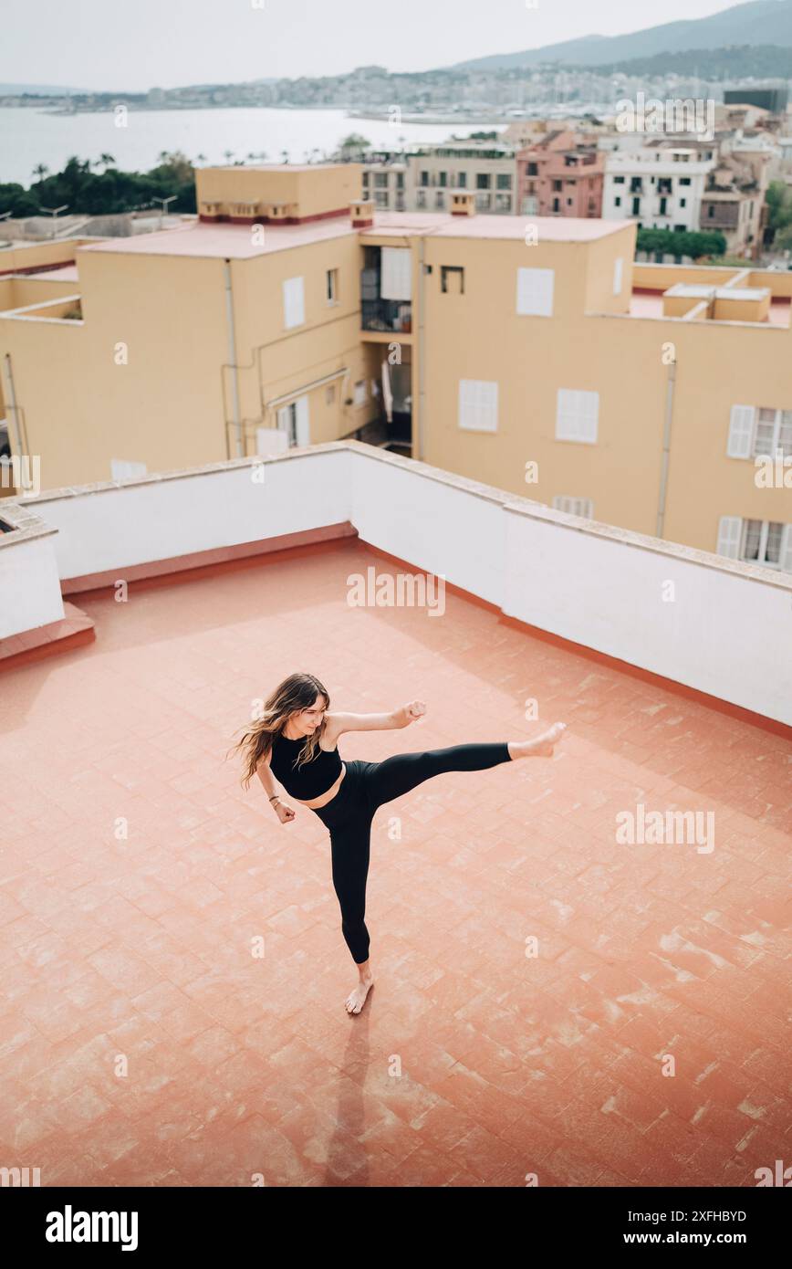 Vista ad alto angolo di una donna determinata che pratica calci alti sulla terrazza dell'edificio Foto Stock