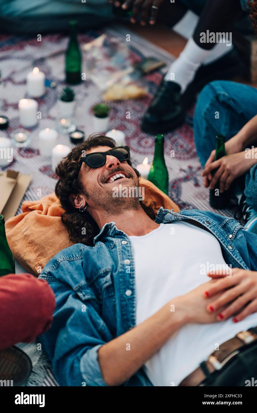 Vista dall'alto dell'uomo sorridente sdraiato sulla coperta da picnic durante la festa sul tetto Foto Stock