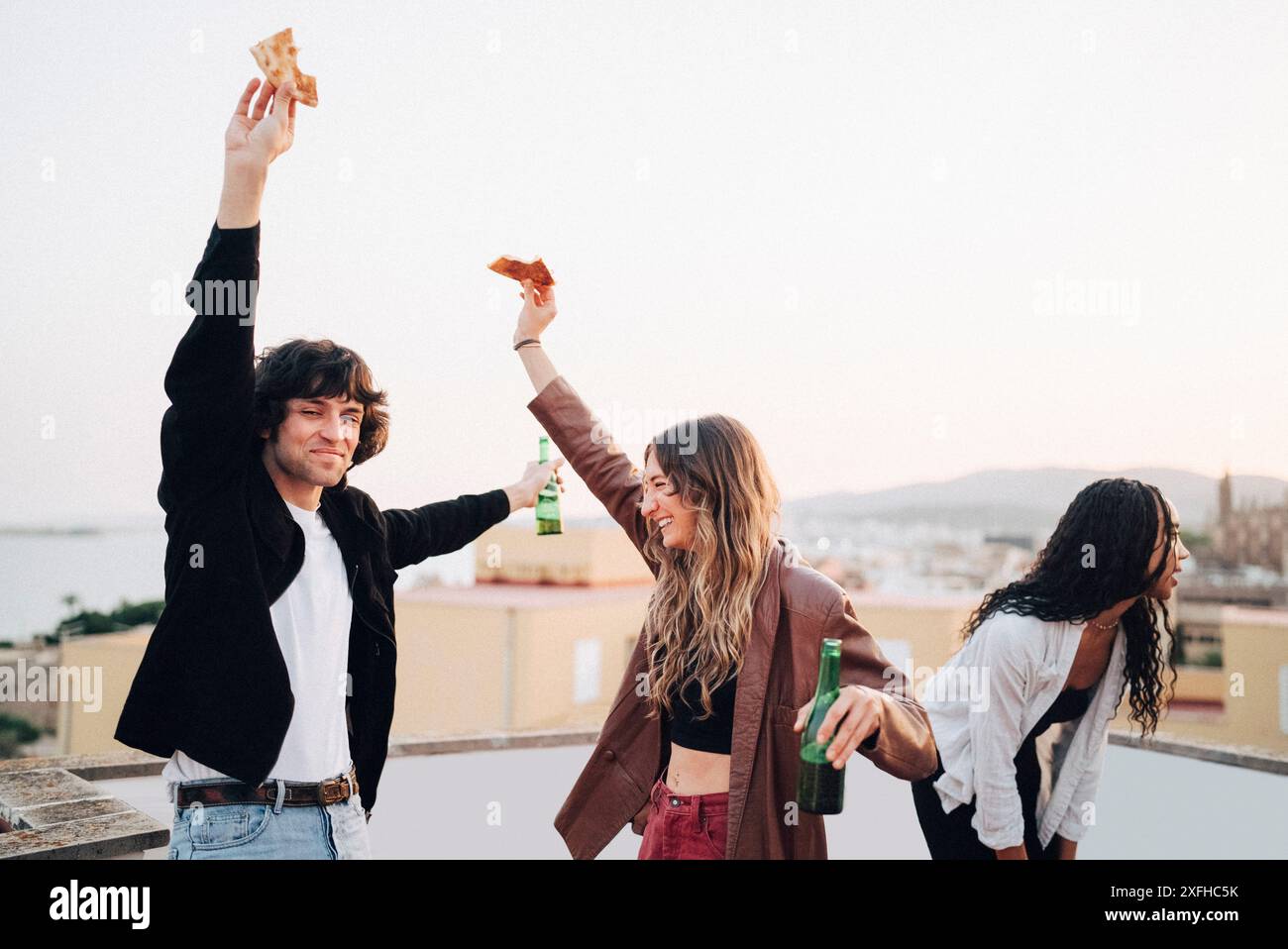 Amici maschili e femminili spensierati che ballano mentre si gusta uno spuntino alla festa sul tetto Foto Stock