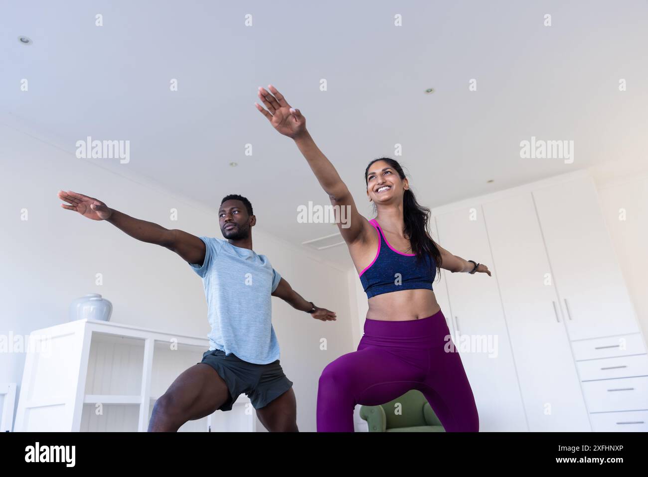 Praticare yoga, uomo e donna che fanno posa guerriera in salotto Foto Stock