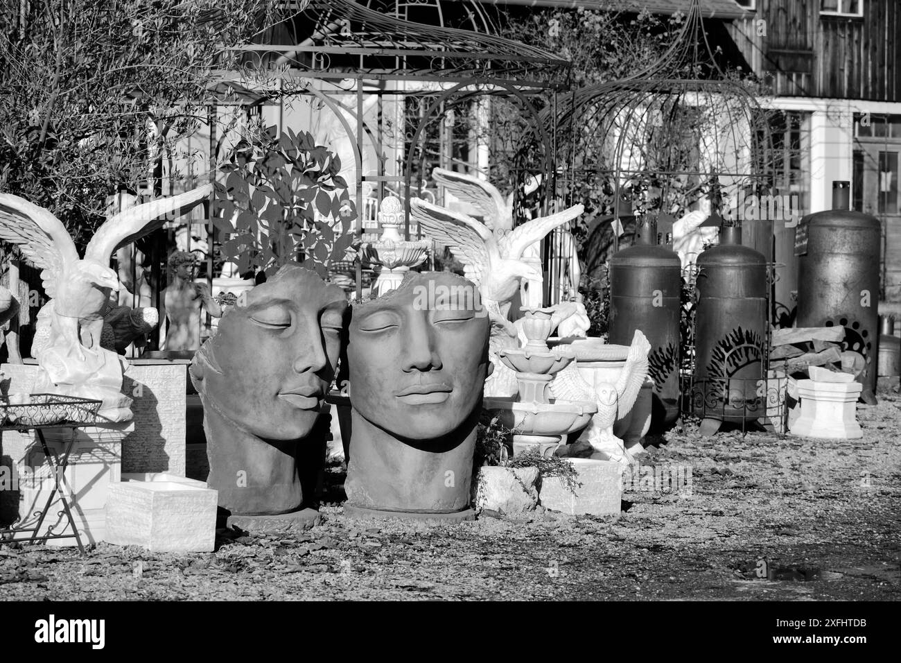 Una foto in bianco e nero di due statue di volti, una delle quali ha una sigaretta in bocca. L'altra statua manca la testa Foto Stock