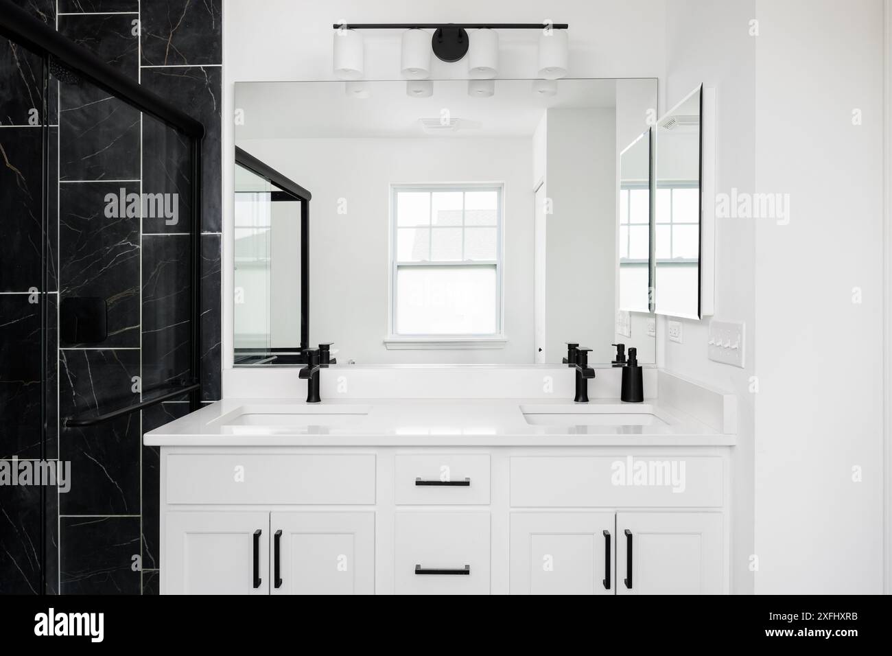 Un bagno bianco con ripiano in marmo, rubinetti neri e una doccia con piastrelle in marmo nero. Foto Stock