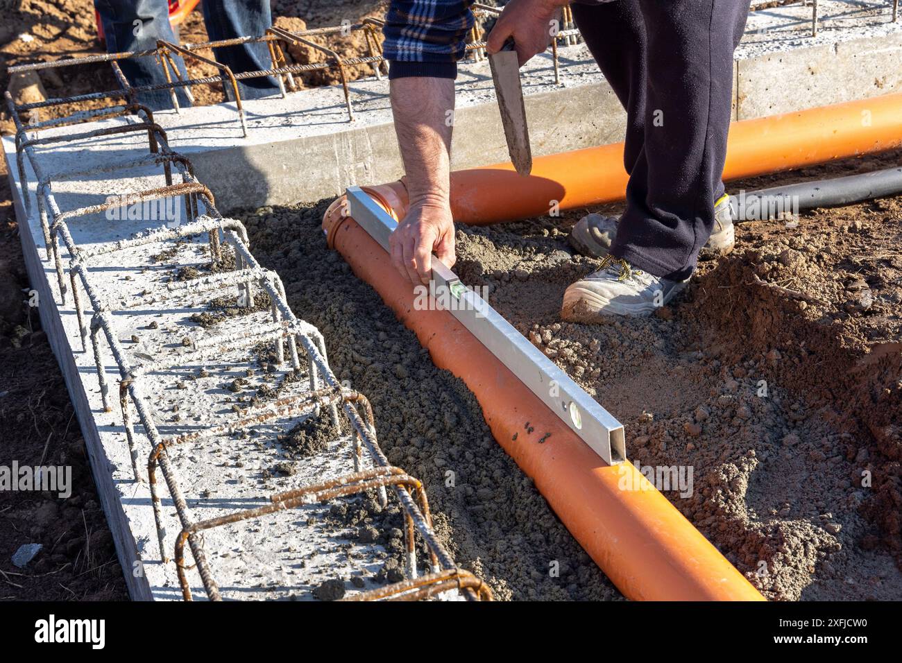 Costruttore edile che misura il livello dei tubi durante la posa e l'installazione di tubi fognari nelle fondamenta di un nuovo edificio Foto Stock