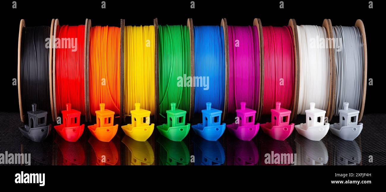 Fila di materiale PLA a filamento per stampa 3d colorato su bobine di cartone riciclabili e ecologiche su backgroun in fibra di carbonio nera Foto Stock