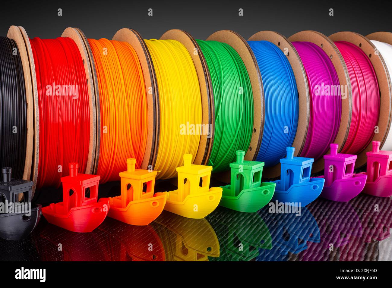 Fila di materiale PLA a filamento per stampa 3d colorato su bobine di cartone riciclabili e ecologiche su backgroun in fibra di carbonio nera Foto Stock