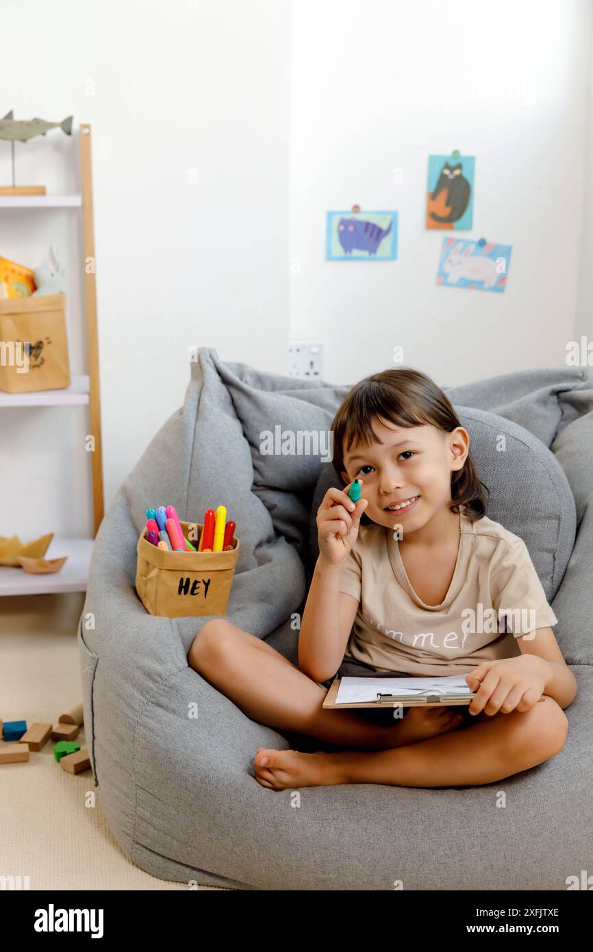 Joyful Boy che gioca con una penna verde in un accogliente spazio interno Foto Stock