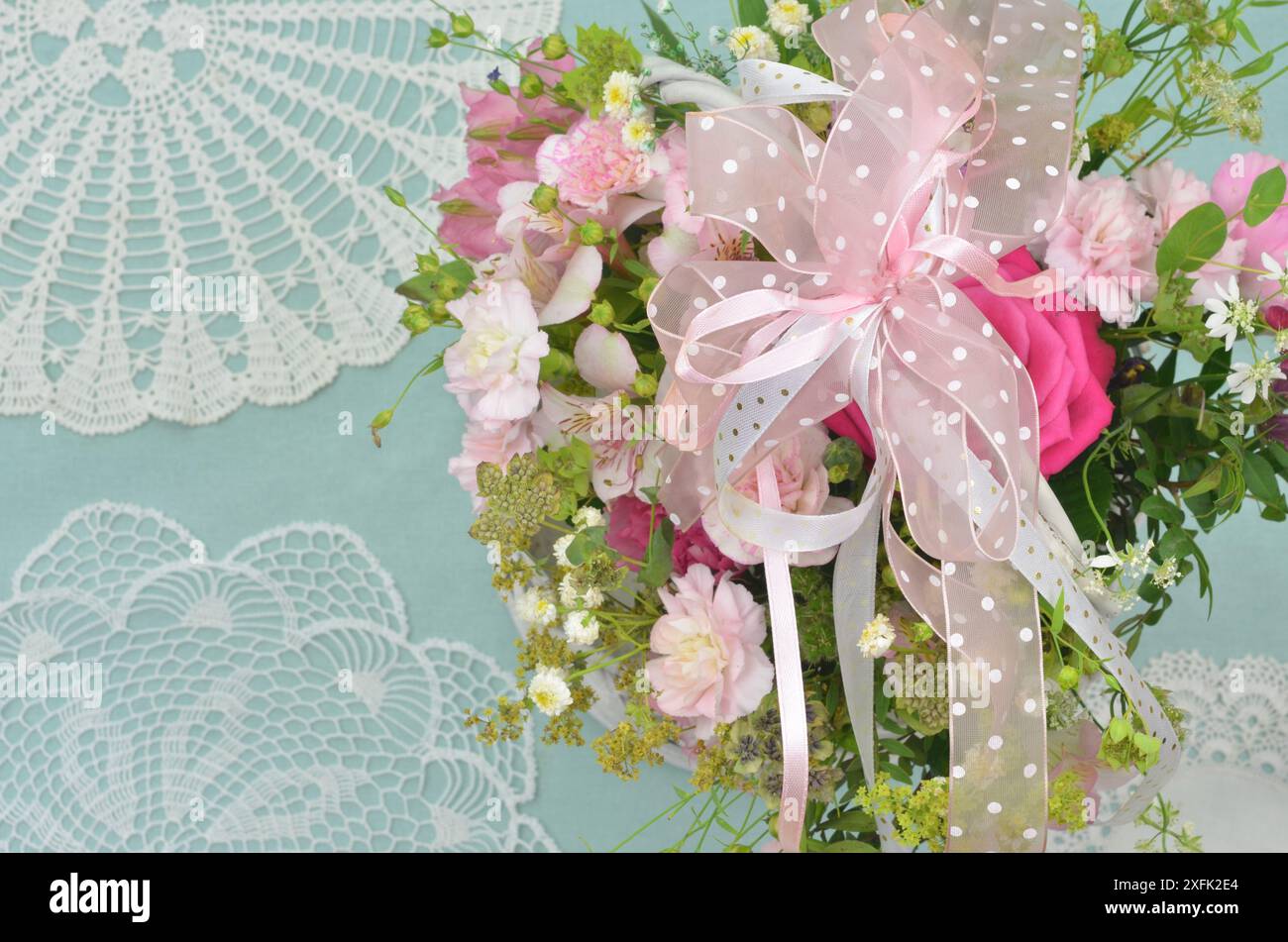 Decorazioni romantiche per matrimoni: Bouquet di fiori rosa e bianchi su tovaglia di menta decorata con motivo regionale a uncinetto. Profondità di campo ridotta. Foto Stock
