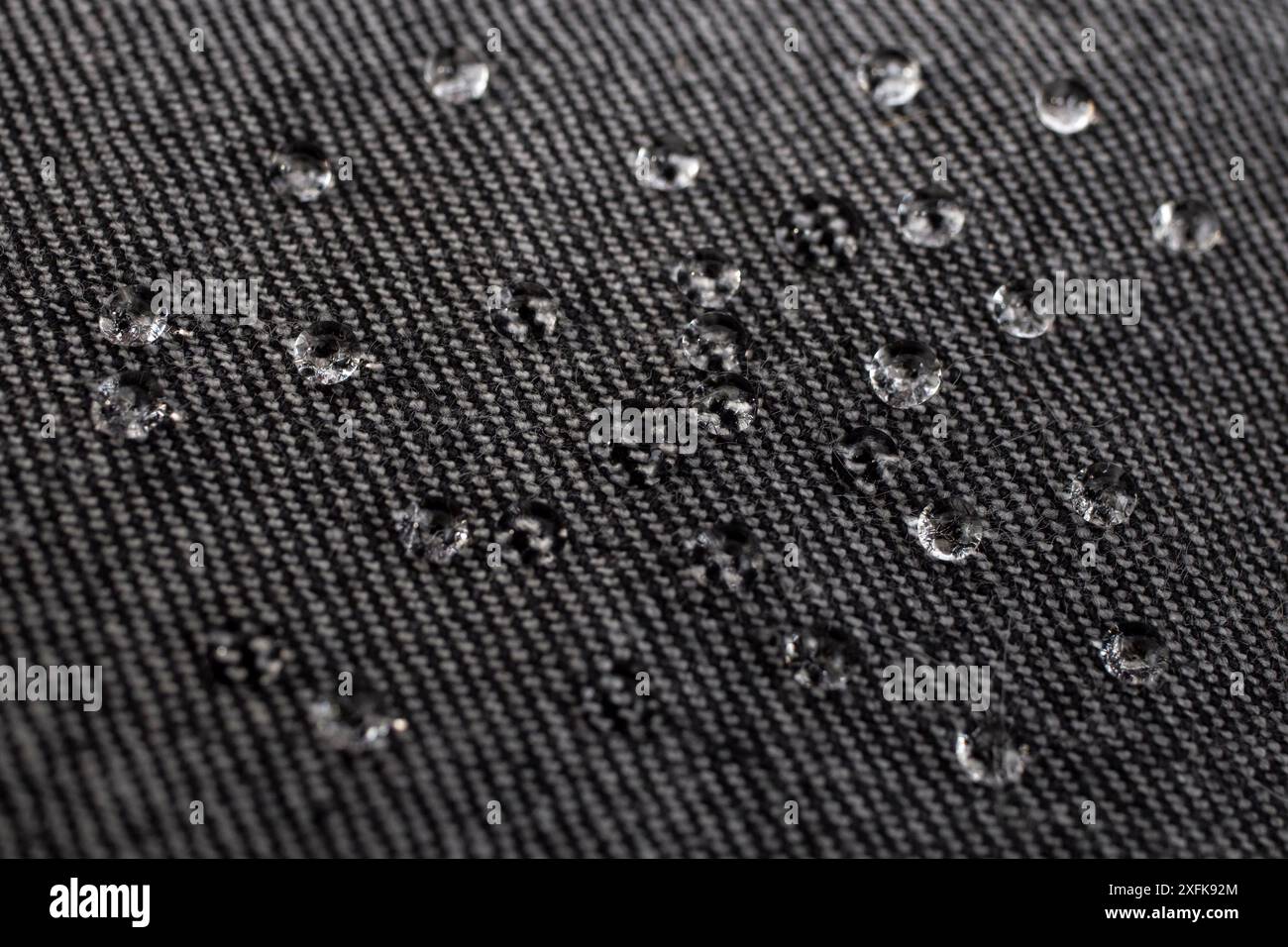 Tessuto jeans nero con gocce d'acqua sulla superficie, concetto di impermeabilità, messa a fuoco morbida Foto Stock