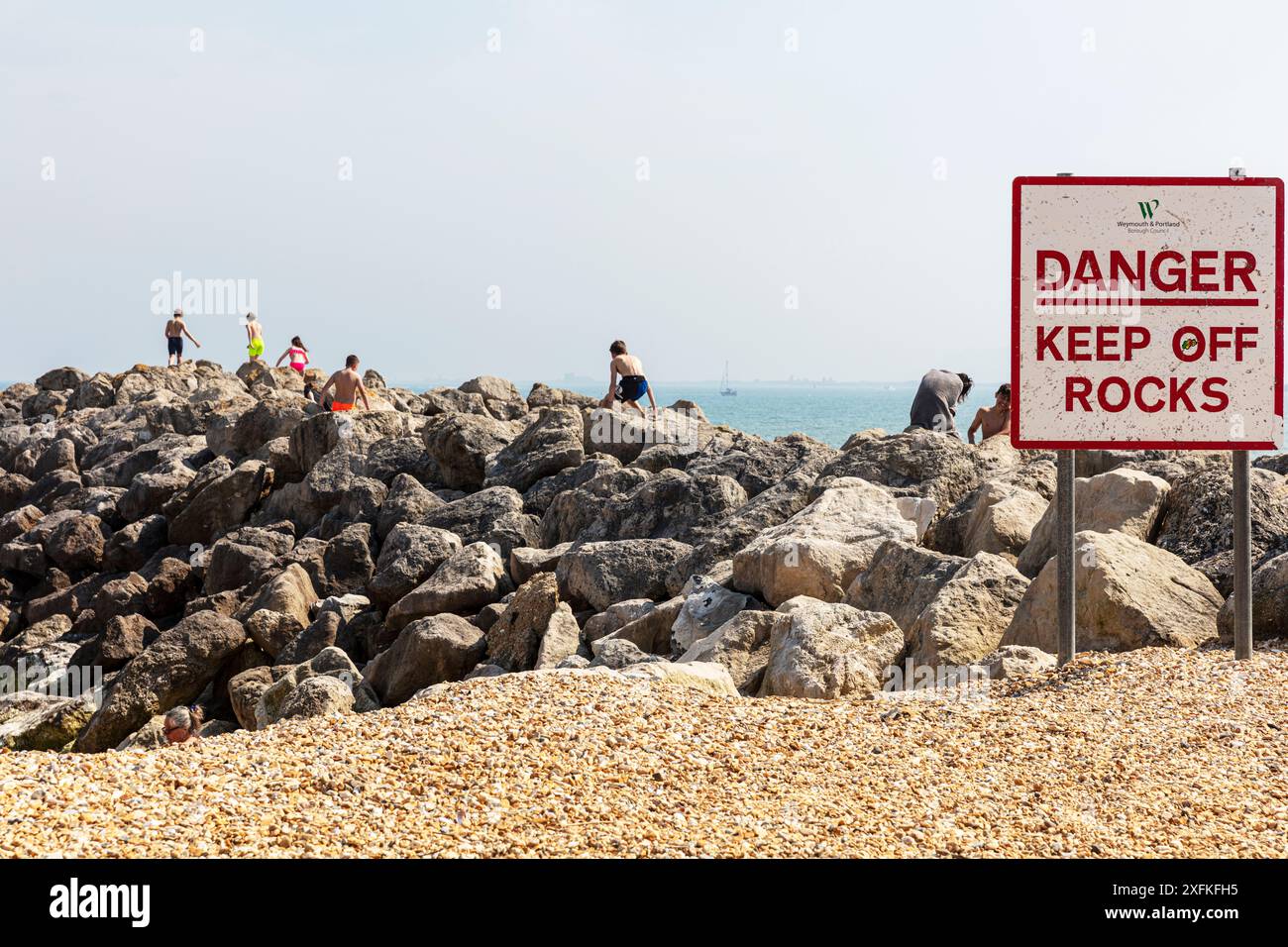 Pericolo, tenere lontano da rocce cartello, Lyme Regis, Dorset, Regno Unito, Inghilterra, bambini che giocano su rocce pericolose, bambini su rocce, bambini che ignorano il cartello, ignorano il cartello, Foto Stock