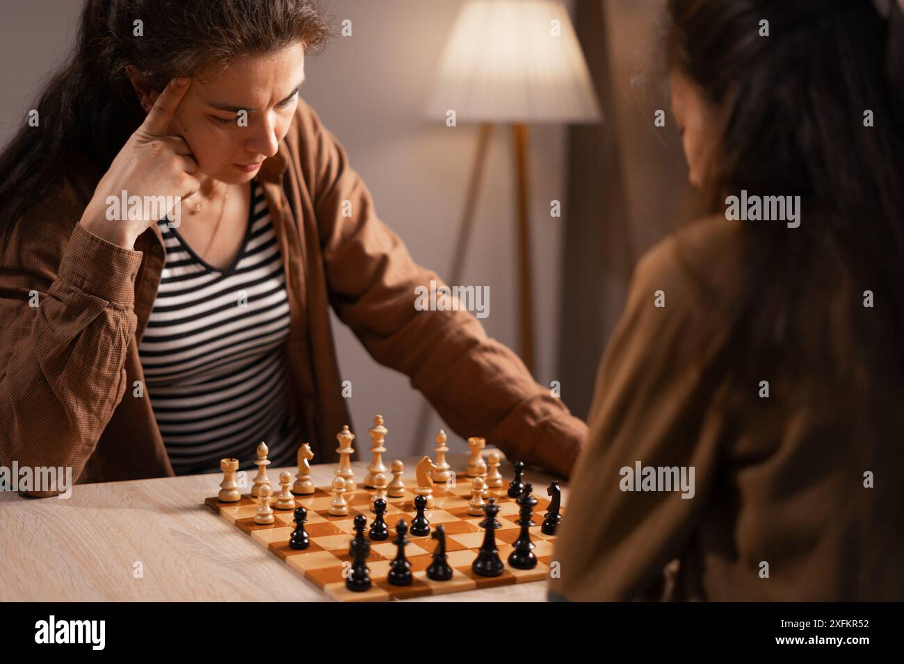 Donna premurosa che gioca a scacchi, pianifica la sua prossima mossa durante una partita con un amico a casa Foto Stock