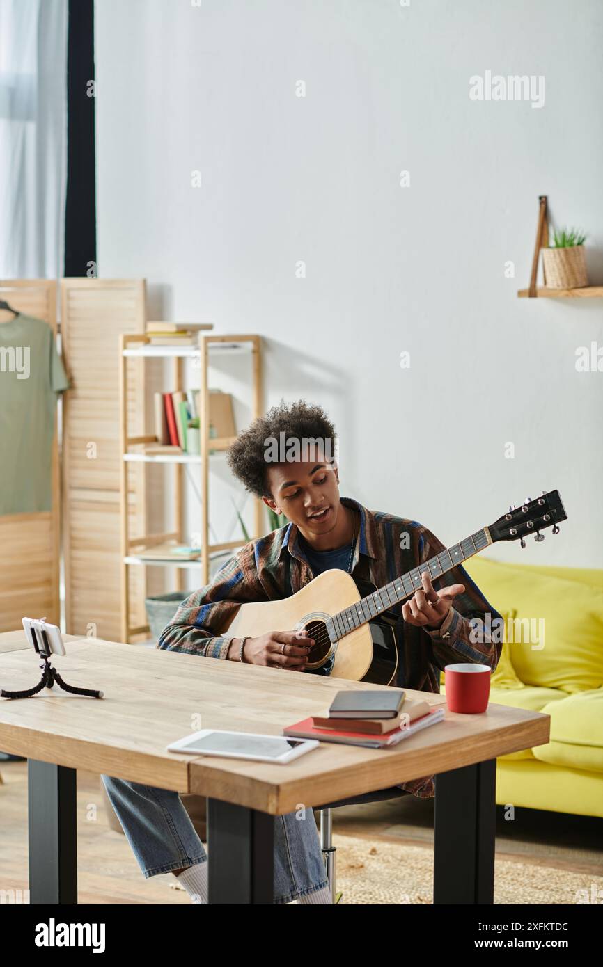 Un uomo di origine afroamericana siede a un tavolo, impegnato a suonare una chitarra acustica. Foto Stock