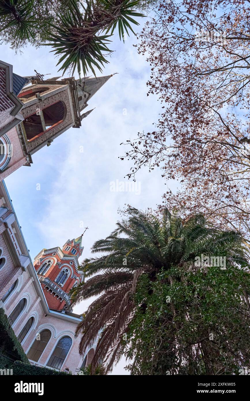 Vista dal basso della chiesa romanica e dell'abbazia di Buenos Aires. Foto scattata dal cortile con palme e querce. C'è una guglia alta, un cr latino Foto Stock