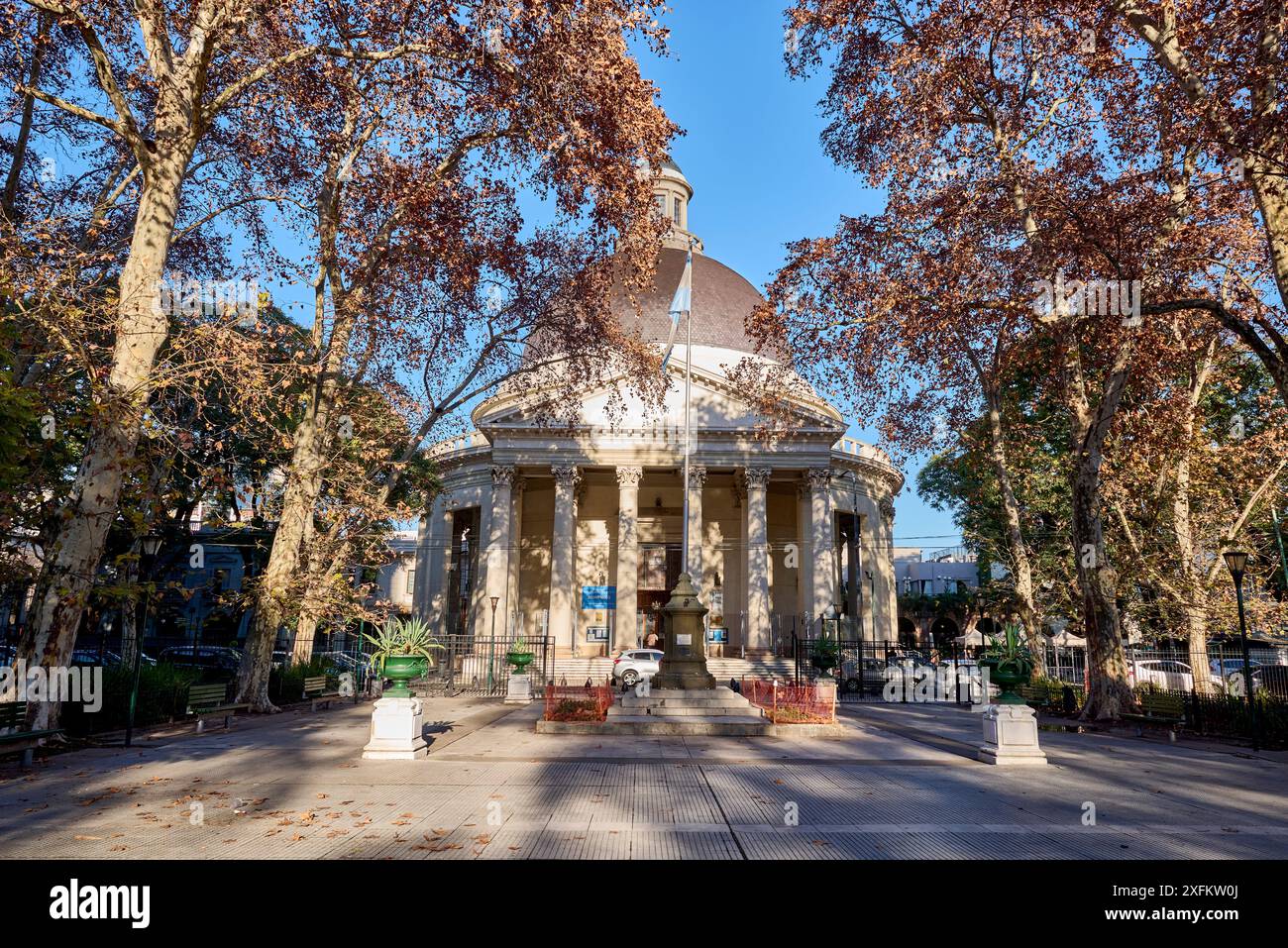 vista autunnale della chiesa con cupola e campanile, ombreggiata da alberi frondosi con foglie secche. Di fronte c'è una piazza con un monumento all'argentino Foto Stock