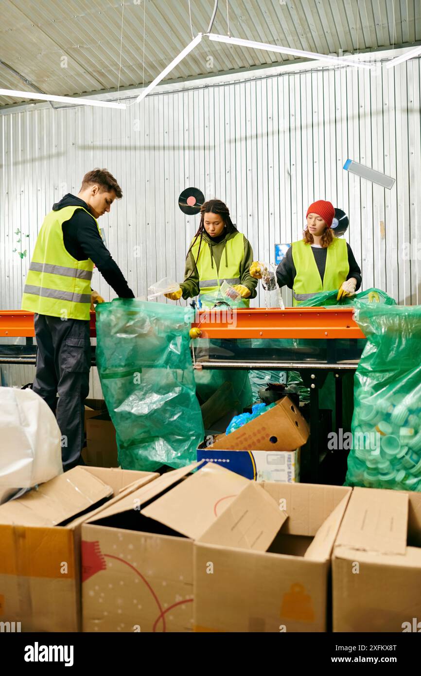 Giovani volontari in guanti e giubbotti di sicurezza lavorano insieme per smistare scatole di rifiuti su un tavolo pieno di articoli da riciclare. Foto Stock