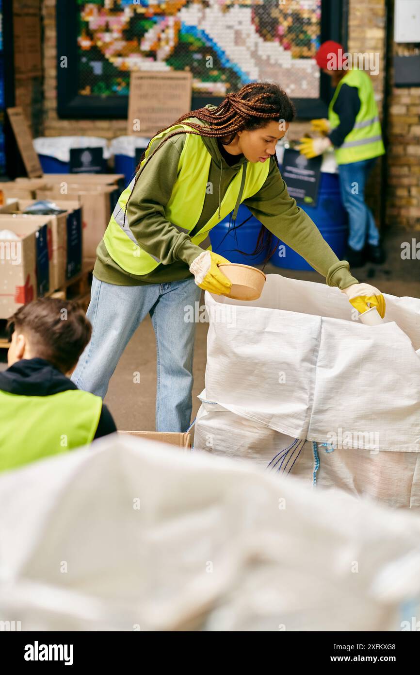 Una donna con una giacca verde aiuta a raccogliere i rifiuti con i giovani volontari in guanti e giubbotti di sicurezza. Foto Stock