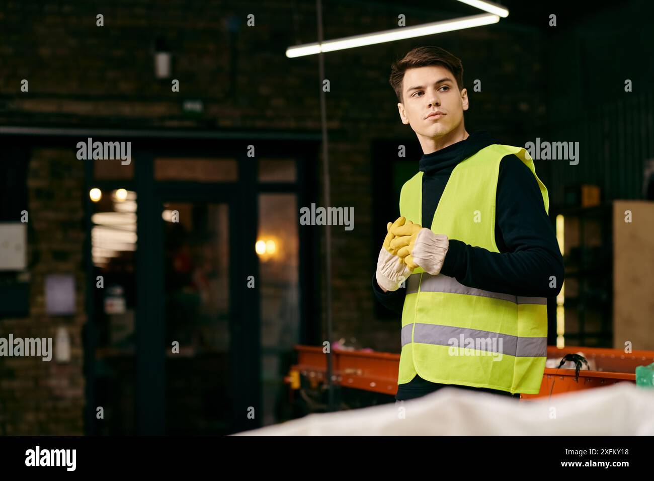 Giovane volontario eco-consapevole in gilet di sicurezza gialli per la selezione dei rifiuti in un magazzino. Foto Stock