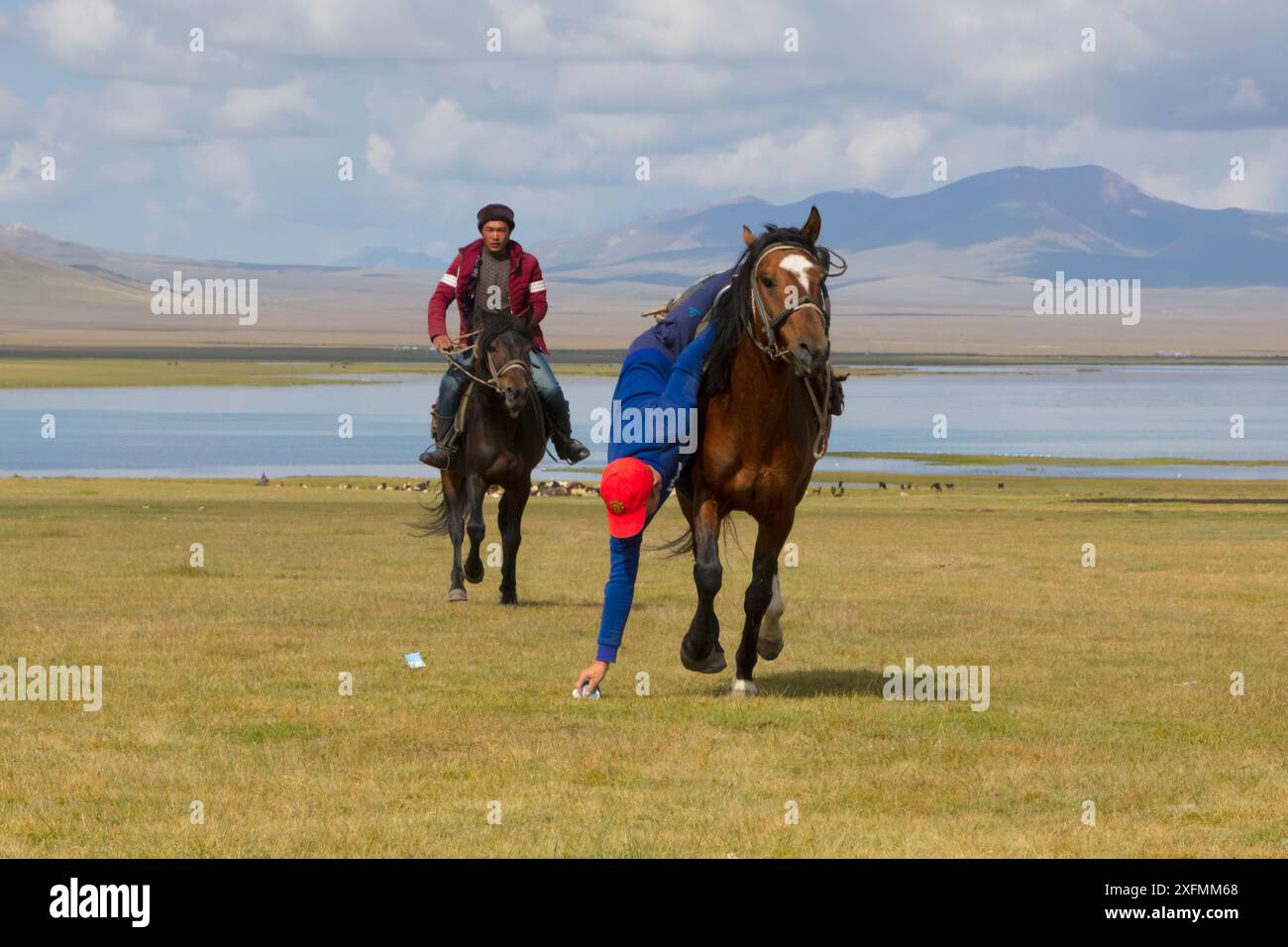 Cavalieri che mostrano abilità nel gioco tradizionale raccogliendo denaro da terra mentre cavalcano, lago Song Kul, Kirghizistan, agosto 2016. Foto Stock