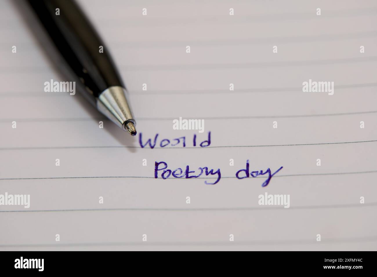 Una penna nera poggia su un pezzo di carta foderata con inchiostro blu, le parole World Poetry Day scritte in corsivo. Foto Stock