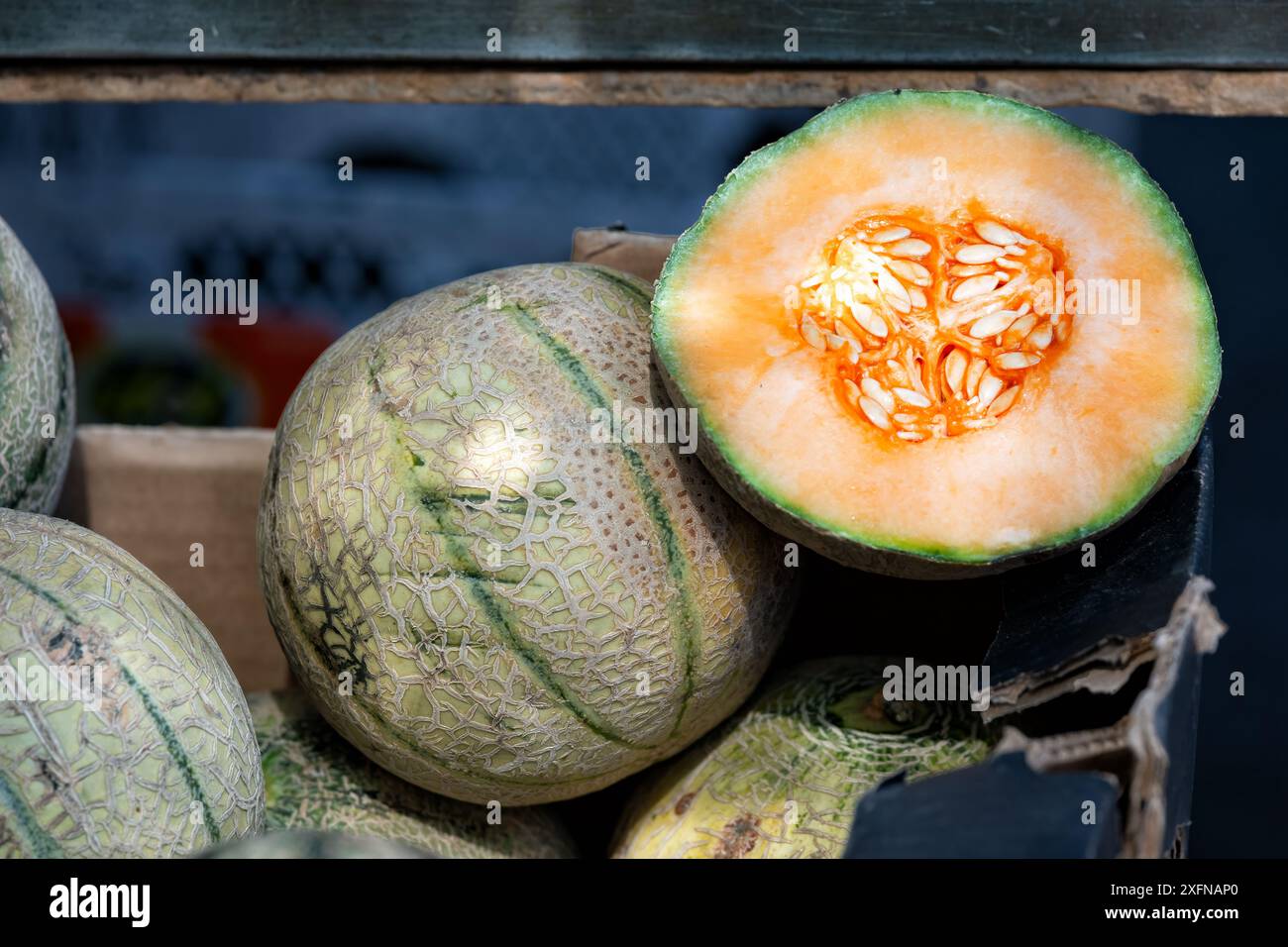 Un melone di cantalopo fresco maturo, tagliato a metà e posto sopra i meloni di cantalopo interi in una bancarella all'aperto. Foto Stock