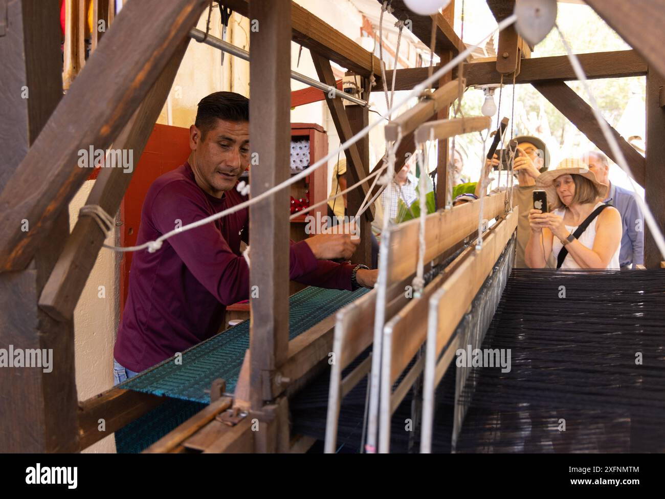 Viaggi in Messico; i turisti osservano un uomo messicano locale che tesseva utilizzando un telaio tradizionale, il Messico. Stile di vita tradizionale messicano Foto Stock